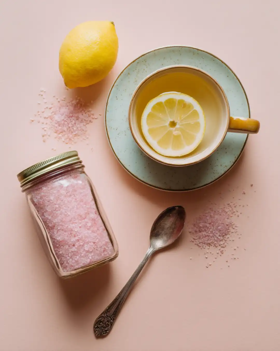 Cup of warm lemon water with Himalayan pink salt and a lemon on a pastel background