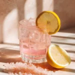 Refreshing glass of pink lemon water with ice, pink salt crystals, and fresh lemon